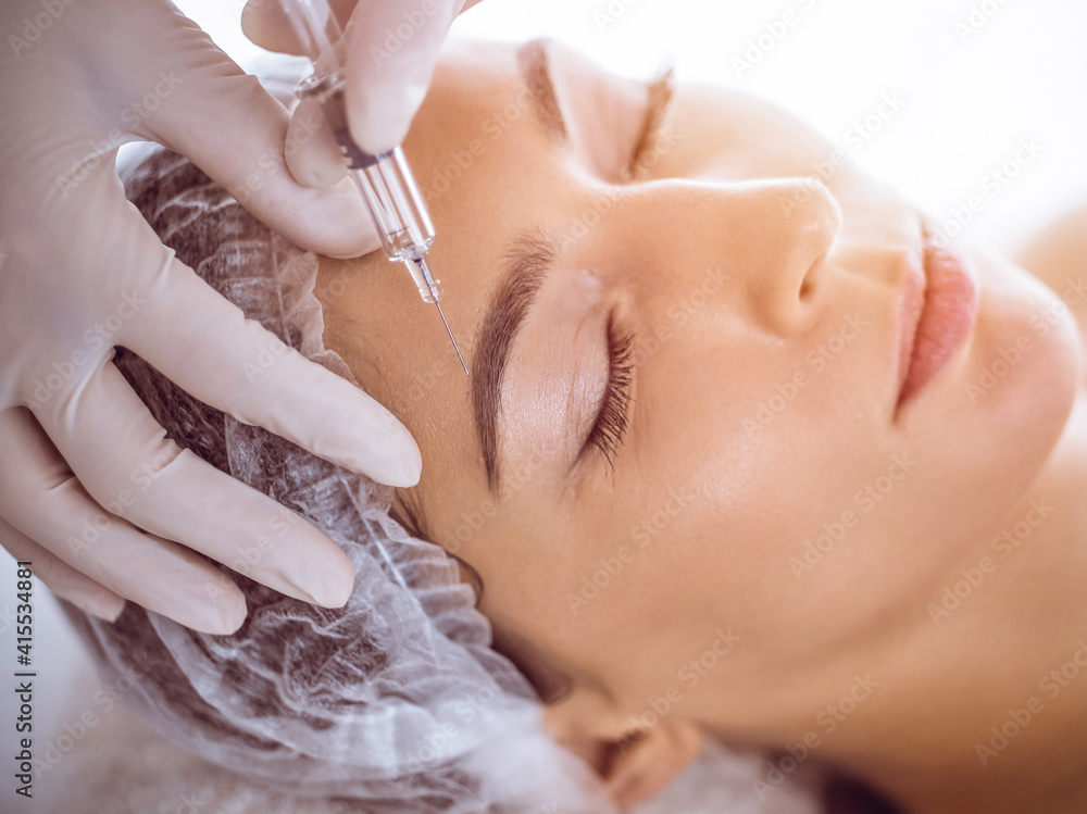 Beautician doing beauty procedure with syringe to face of young brunette woman in sunny spa center. Cosmetic medicine and surgery, beauty injections