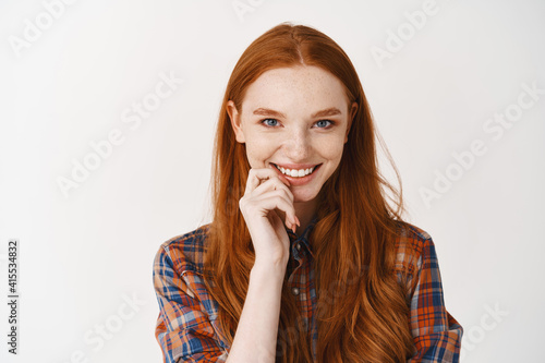 Close-up of silly redhead girl looking at camera  smiling with white teeth and happy face  standing over white background