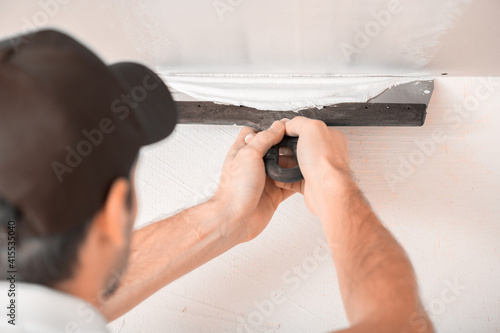 A man uses a spatula to putty a drywall joint on the ceiling Close up