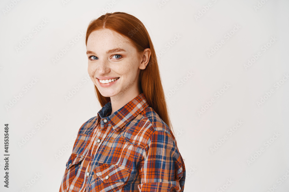 Image of young happy redhead woman with pale skin and no make-up, smiling at camera, standing over white background Image of young happy redhead woman with pale skin and no make-up, smiling at camera, standing over white background