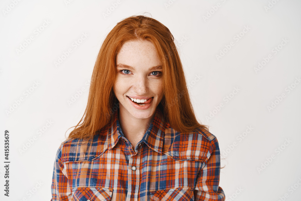 Beautiful ginger girl with blue eyes and flirty smile, showing tongue and looking flirty at camera, standing over white background Beautiful ginger girl with blue eyes and flirty smile, showing tongue and looking flirty at camera, standing over white background