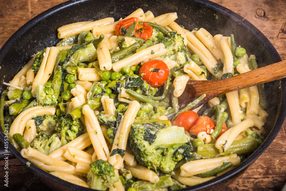 Vegetarian american and italian primavera pasta dish with broccoli, beans, asparagus, peas and tomatoes in a frying pan on a wooden table, top view Vegetarian american and italian primavera pasta dish with broccoli, beans, asparagus, peas and tomatoes in a frying pan on a wooden table, top view