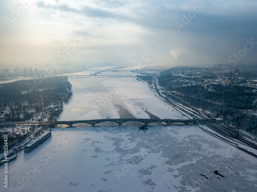 The frozen Dnieper river in Kiev. Aerial drone view. Winter frosty morning. The sun breaks through the clouds. © Sergey