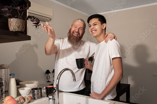 Obraz na płótnie Happy smiling dad and son talking on kitchen at home. Father showing son something and laughing. Concept of relationship between parents and children teenagers. w salonie