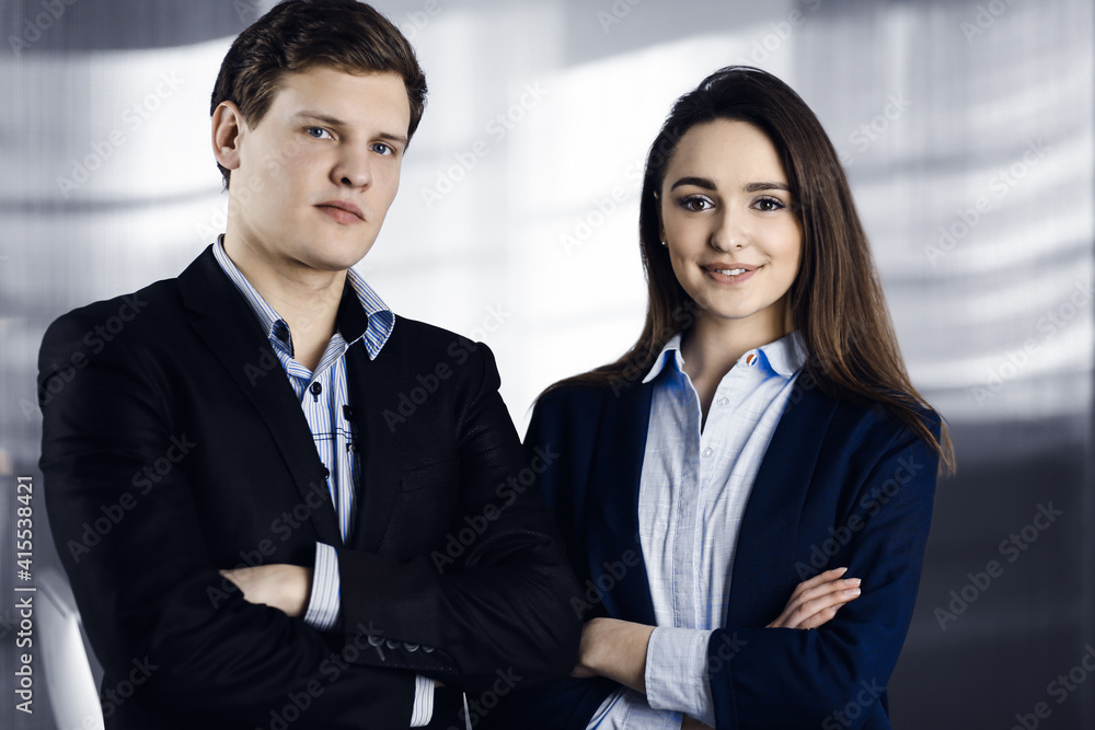 Friendly young colleagues are standing as a team with crossed arms in a modern office. Portrait of successful business people at work Friendly young colleagues are standing as a team with crossed arms in a modern office. Portrait of successful business people at work