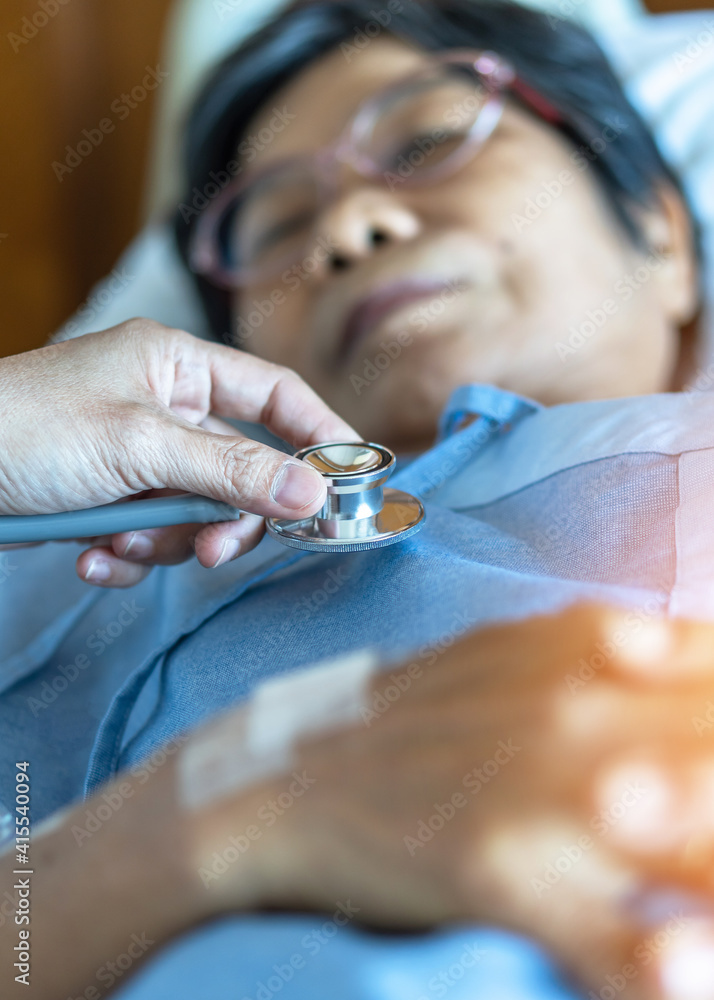 Hospitalized elderly patient, senior old aging woman laying on bed with cardiologist doctor or physician examining cardiological heart health, checking pulse in hospital clinic exam room