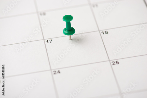 Cropped close up view photo of green thumbtack attached to the white blank empty calendar