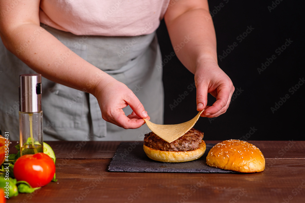 A close-up of a delicious burger being prepared. The cook puts a slice of cheese on a juicy cutlet. Gastronomy, recipes, menus, fast food. Juicy burger