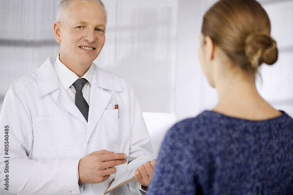 Fototapeta premium Elderly confident doctor consults woman patient in clinic. Perfect medical service in hospital. Medicine and healthcare concept