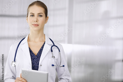 Cheerful female doctor standing in clinic. Portrait of friendly smiling woman physician. Perfect medical service in hospital. Medicine concept