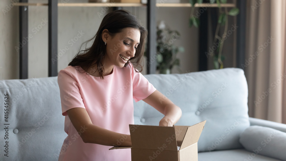 Hopeful excited young mixed race female prepare moving relocation to new house pack things to cardboard box. Curious arabian woman customer of internet store receive unpack parcel with consumer goods