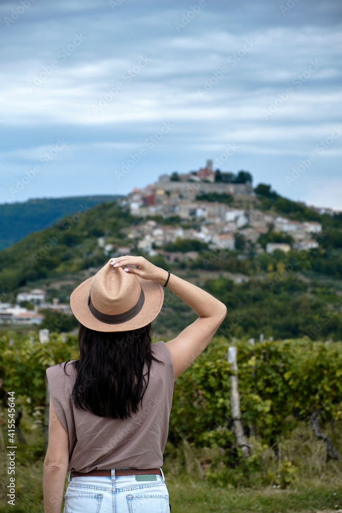 Motovun, Croatia. Girl in a straw hat siting in vineyards with view of Motovun in Croatia. 
