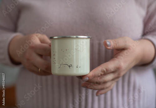 Metal mug filled with hot coffee with cinnamon and milk foam.