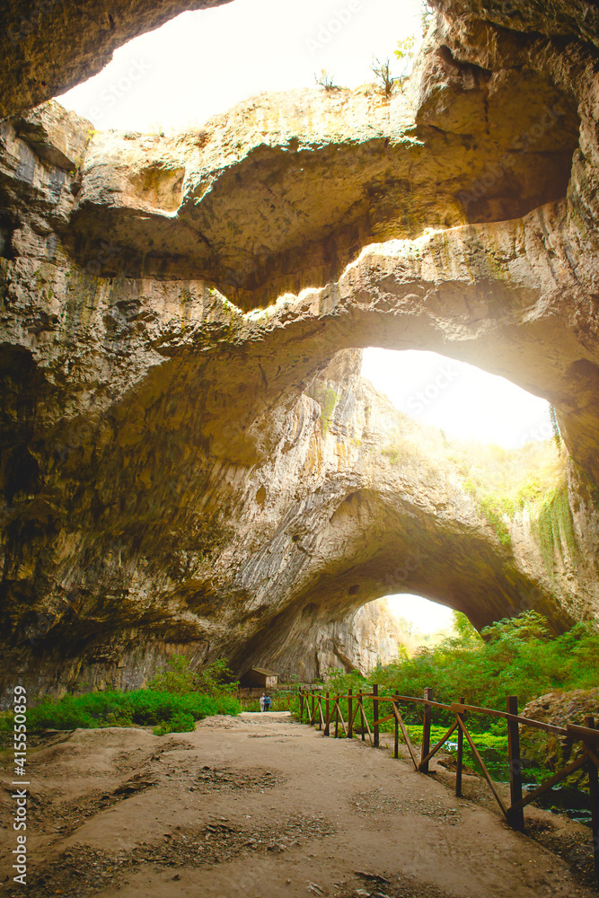 Devetashka cave in Bulgaria - natural attraction. High arches of a huge stone cave with round holes at the top, a tourist road with a fence inside the cave. 