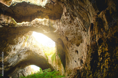 Wallpaper Mural Devetashka cave in Bulgaria - natural attraction. High arches of a huge stone cave with round holes at the top, a tourist road with a fence inside the cave.  Torontodigital.ca