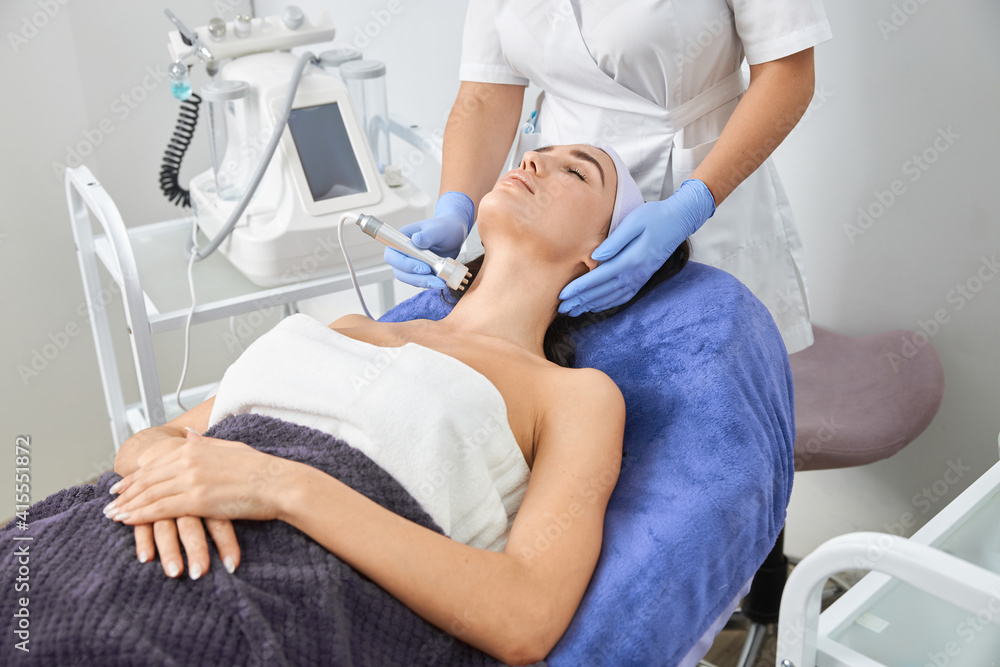 Professional cosmetologist is doing procedures for client in light cabinet Professional cosmetologist is doing procedures for client in light cabinet