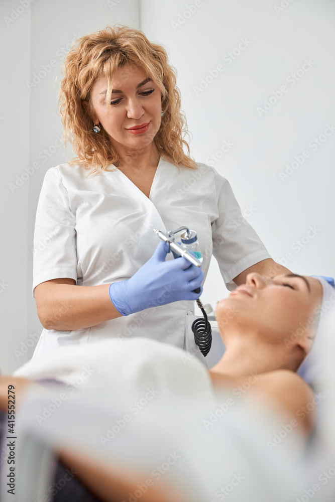 Fototapeta premium Professional cosmetologist is doing procedures for client in light cabinet