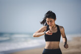 Well being sport concept, Asian muscular healthy woman jogging running looking at smart watch on beach