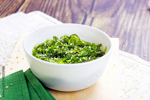 Green Asian seaweed salad in a white bowl on wooden background.