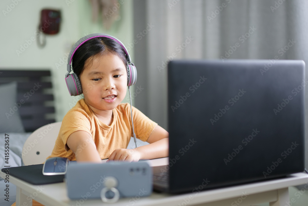 Asian child or kid girl smile e-learning on computer notebook and smartphone to wearing headphone for live streaming or video call by enjoy study online or people learn from home school to play laptop Asian child or kid girl smile e-learning on computer notebook and smartphone to wearing headphone for live streaming or video call by enjoy study online or people learn from home school to play laptop