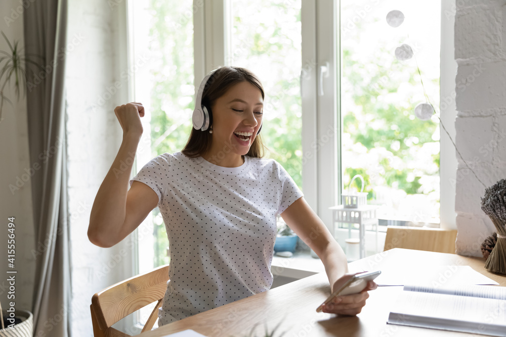 Excited millennial Caucasian female in headphones triumph win online lottery on smartphone. Happy overjoyed young woman in earphones feel euphoric read good news on cellphone. Luck concept. Excited millennial Caucasian female in headphones triumph win online lottery on smartphone. Happy overjoyed young woman in earphones feel euphoric read good news on cellphone. Luck concept.
