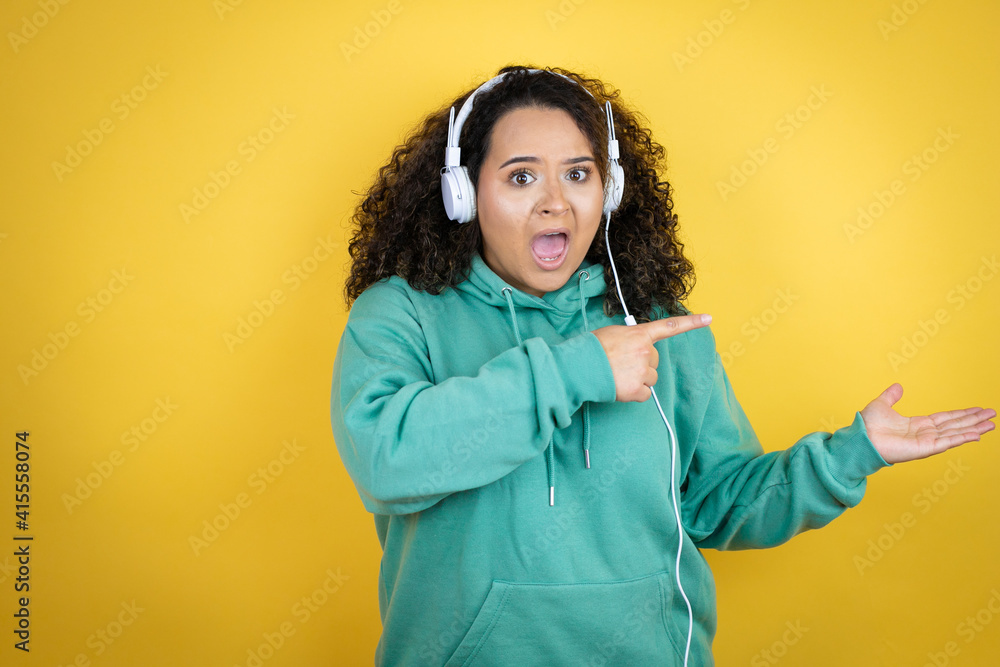 Young african american girl wearing gym clothes and using headphones surprised, showing and pointing something that is on her hand Young african american girl wearing gym clothes and using headphones surprised, showing and pointing something that is on her hand