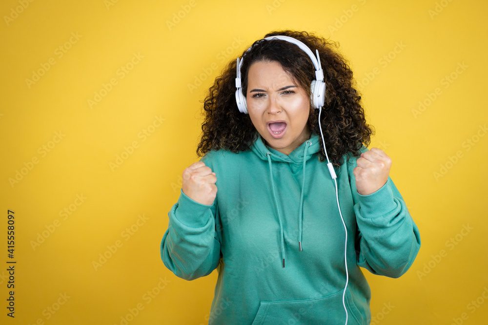 Young african american girl wearing gym clothes and using headphones very happy and excited making winner gesture with raised arms, smiling and screaming for success. Young african american girl wearing gym clothes and using headphones very happy and excited making winner gesture with raised arms, smiling and screaming for success.