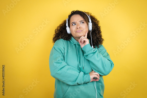 Young african american girl wearing gym clothes and using headphones with hand on chin thinking about question, pensive expression. smiling and thoughtful face. doubt concept.