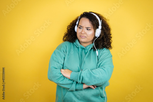 Young african american girl wearing gym clothes and using headphones thinking looking tired and bored with crossed arms
