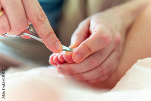 Woman's hands with scissors for cutting nails counting the toenails of baby six months. baby care concept