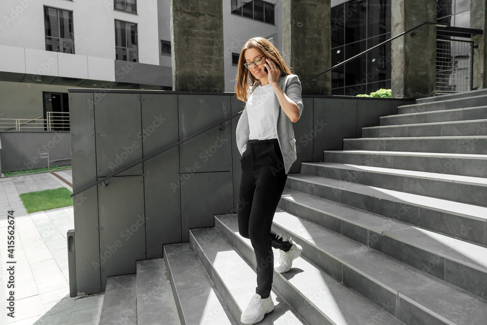 Fototapeta premium Young woman going downstairs talking on smartphone