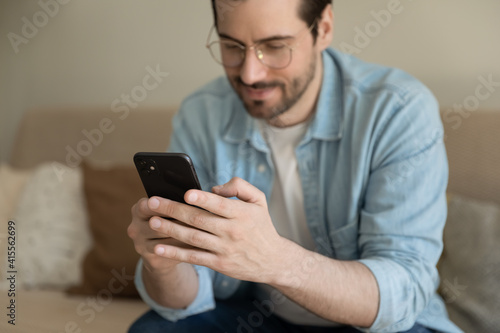Close up of millennial Caucasian man sit at couch at home texting messaging online on smartphone. Young 20s male relax at home browse surf wireless internet on modern cellphone. Communication concept.