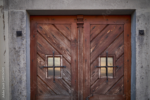 Close-up of old wooden doors with window, sunset reflection and walls around