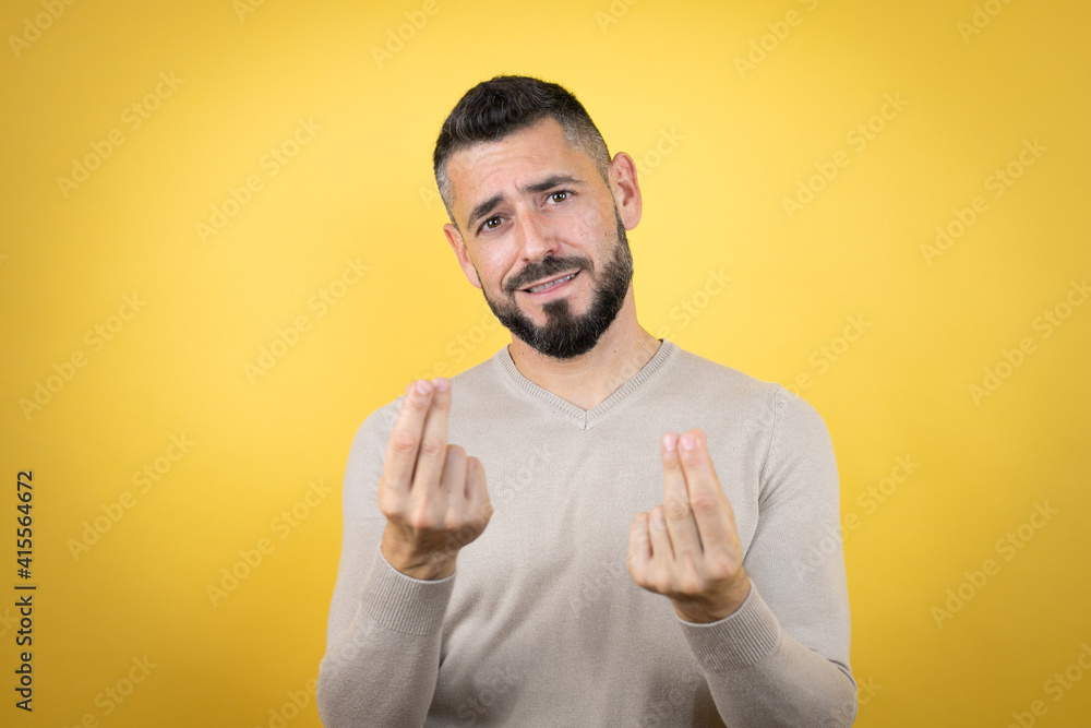 Handsome man with beard wearing sweater over yellow background doing money gesture with hands, asking for salary payment, millionaire business Handsome man with beard wearing sweater over yellow background doing money gesture with hands, asking for salary payment, millionaire business