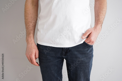 Legs of a young man in jeans with a hand in a pocket on a gray background.