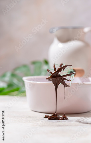 Dark melted chocolate on a whisk in a white bowl on a light background. Handmade chocolate making, dessert concept. © Gulsina