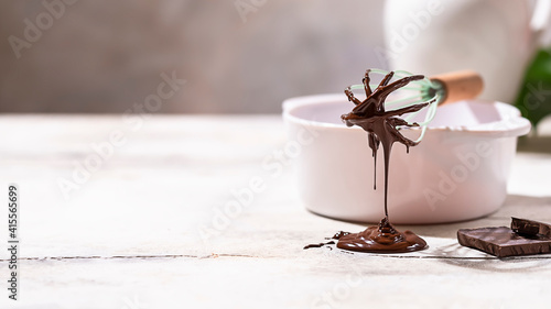 Dark melted chocolate on a whisk in a white bowl on a light background. Handmade chocolate making, dessert concept. © Gulsina