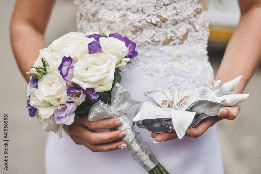 The bride is holding a bouquet of flowers and two wedding rings. Wedding bouquet and gold rings. The bride is holding a bouquet of flowers and two wedding rings. Wedding bouquet and gold rings.