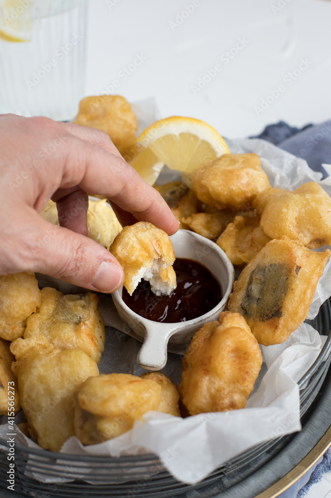 A piece of tempura hake held by a man hand about to be spread with barbecue sauce. A piece of tempura hake held by a man hand about to be spread with barbecue sauce.