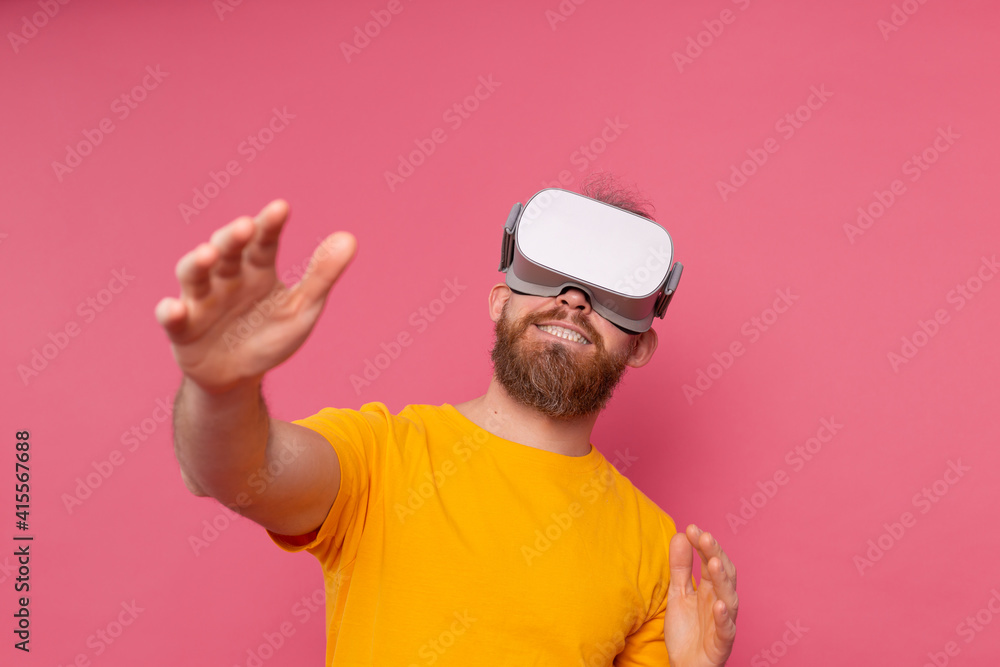 Handsome positive bearded man touching air in vr glasses studio background