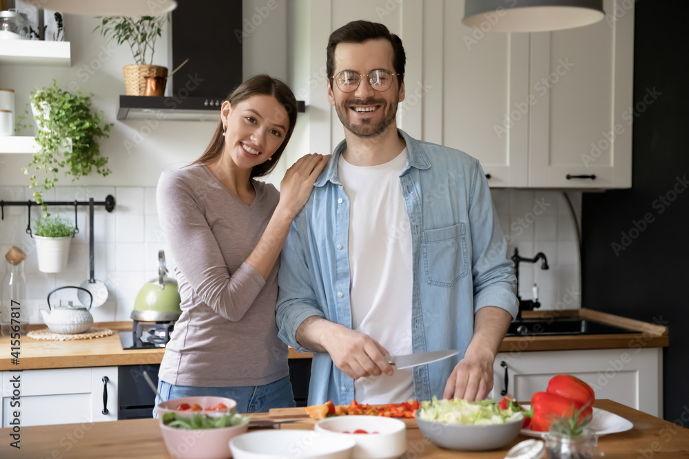 Portrait of happy young family pose in modern cozy home kitchen preparing healthy vegetarian salad. Smiling millennial couple renters cooking delicious diet food in the morning in own modern house. Portrait of happy young family pose in modern cozy home kitchen preparing healthy vegetarian salad. Smiling millennial couple renters cooking delicious diet food in the morning in own modern house.