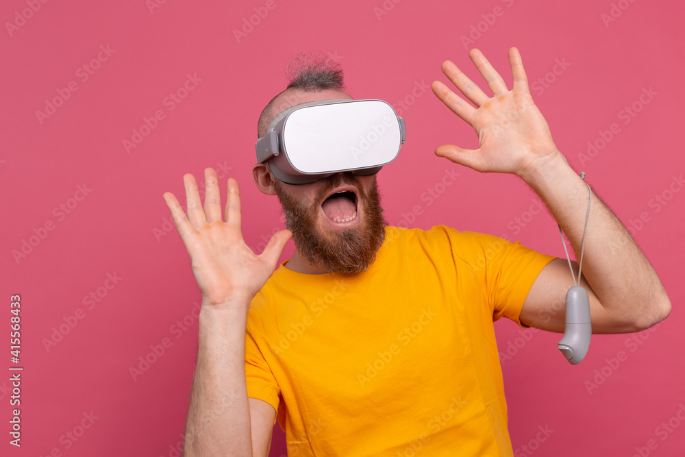 Portrait of scared gamer, man with beard in t-shirt wearing vr glasses on studio background Portrait of scared gamer, man with beard in t-shirt wearing vr glasses on studio background