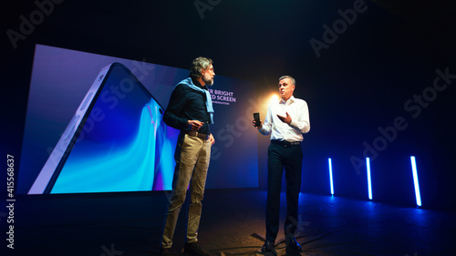 Foto Male speakers discussing new smartphone on stage