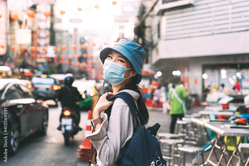 Walking young adult asian woman backpack traveller wear face mask for corona virus or covid-19. People traveling in city lifestyle at outdoor at China town street food market. Bangkok, Thailand Walking young adult asian woman backpack traveller wear face mask for corona virus or covid-19. People traveling in city lifestyle at outdoor at China town street food market. Bangkok, Thailand