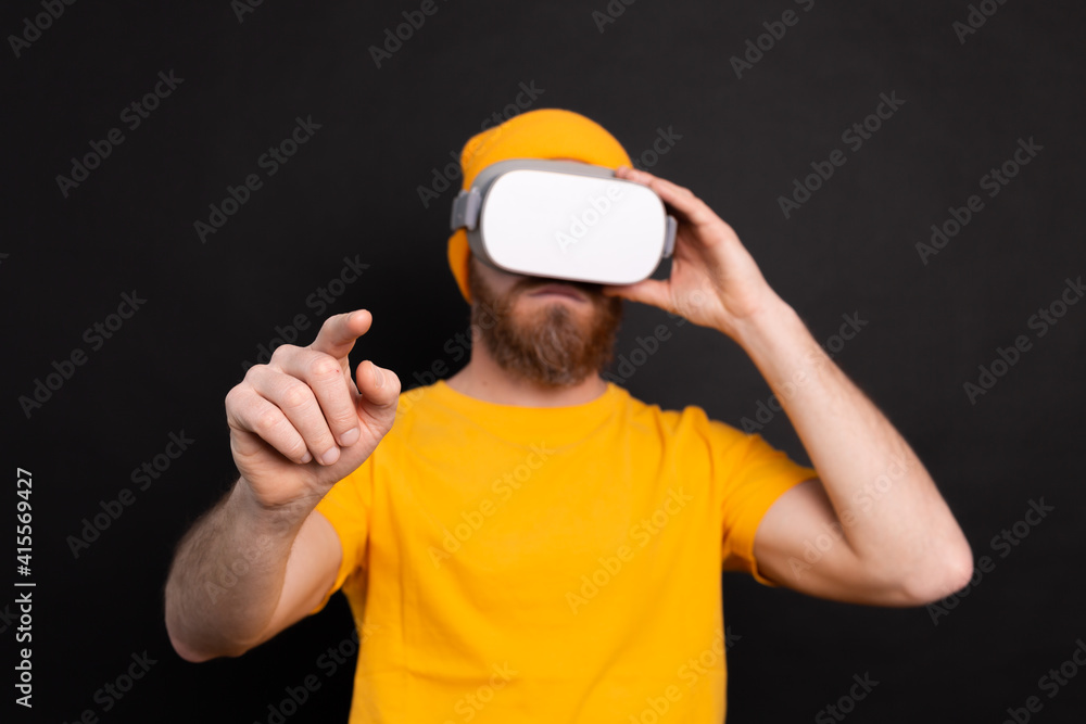 Handsome positive bearded man touching air in vr glasses studio background