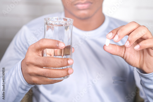  young man holding pills and glass of water with copy space 