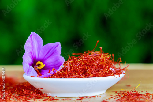 Dry saffron stigmas and a single crocus flower in a white plate on a wooden surface. Saffron spice. photo