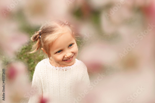 Blonde little girl photographed through the flowering branches of a tree. A child in a spring flower garden  © Maryana