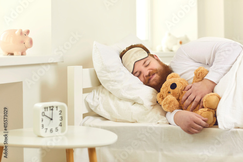 Fotografi Happy grown-up man sleeping in good comfortable bed with cute teddy bear