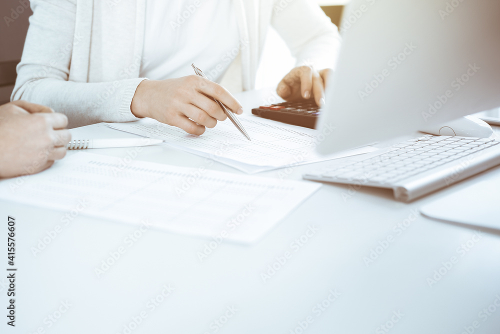 Accountant checking financial statement or counting by calculator income for tax form, hands close-up. Business woman sitting and working with colleague at the desk in office. Audit concept Accountant checking financial statement or counting by calculator income for tax form, hands close-up. Business woman sitting and working with colleague at the desk in office. Audit concept